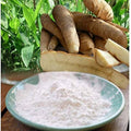 Raw yams on a wooden board with a bowl of white powder in front, against a green leafy background.