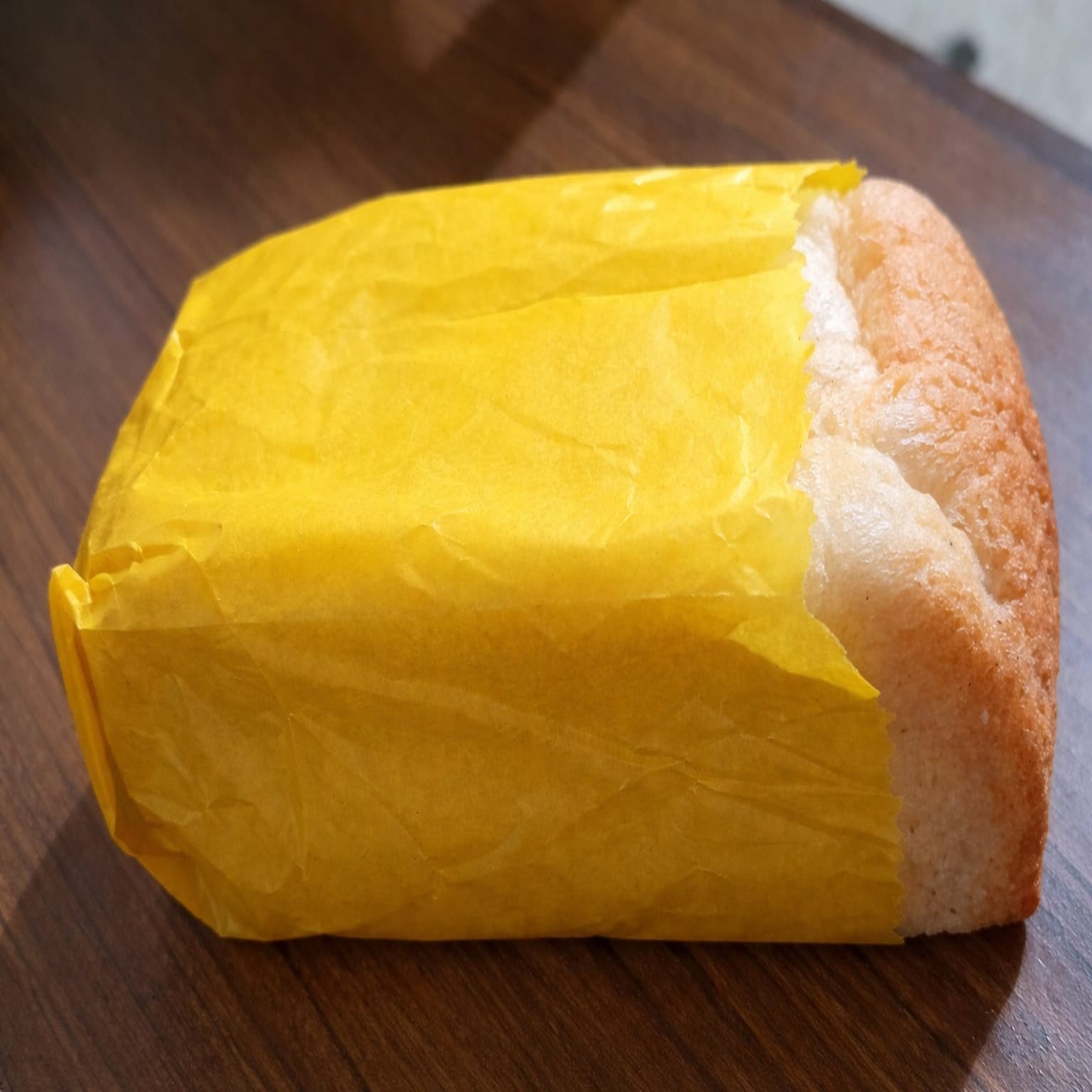 Loaf of bread wrapped in yellow paper on a wooden surface